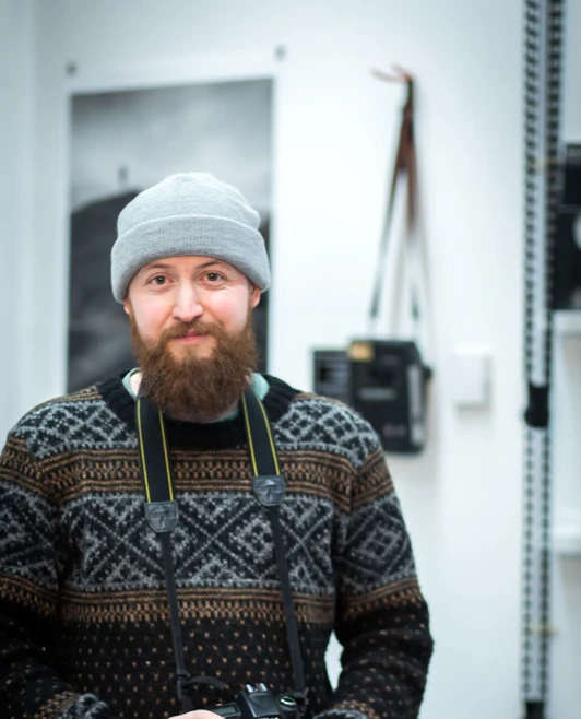 Bearded student holding a Nikon DSLR camera and smiling in a photography studio. Bearded student holding a Nikon DSLR camera and smiling in a photography studio.